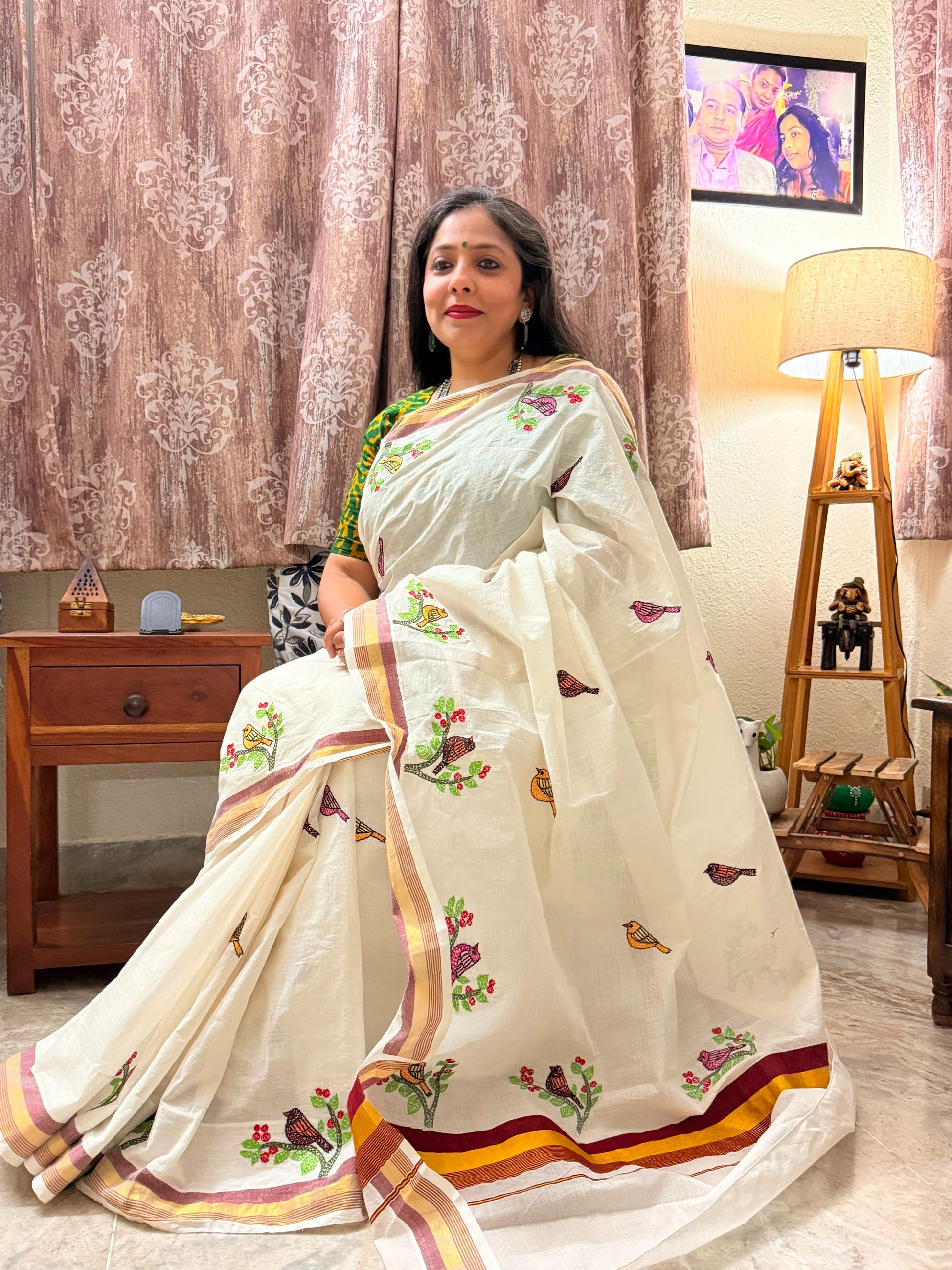 Woman draped in ivory Kerala Cotton Saree featuring colourful Sujni embroidered bird motifs and traditional gold border