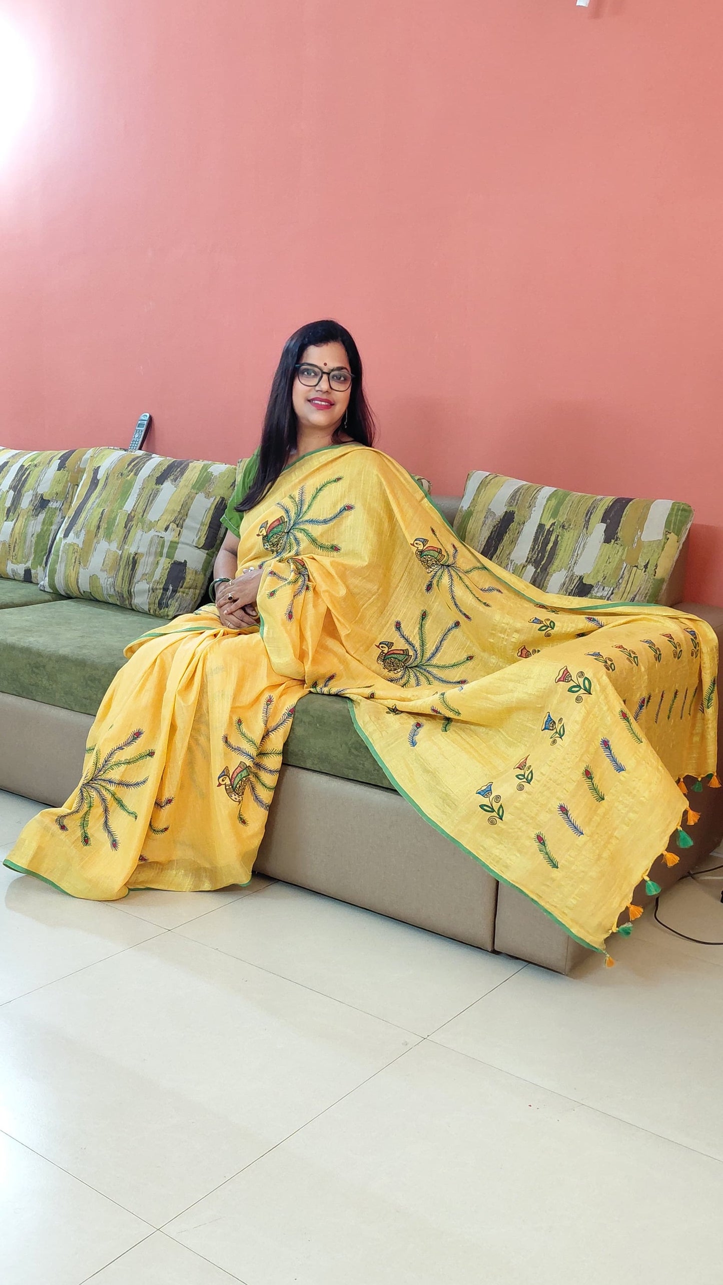 Woman in a yellow saree sitting on a couch with a pink wall background