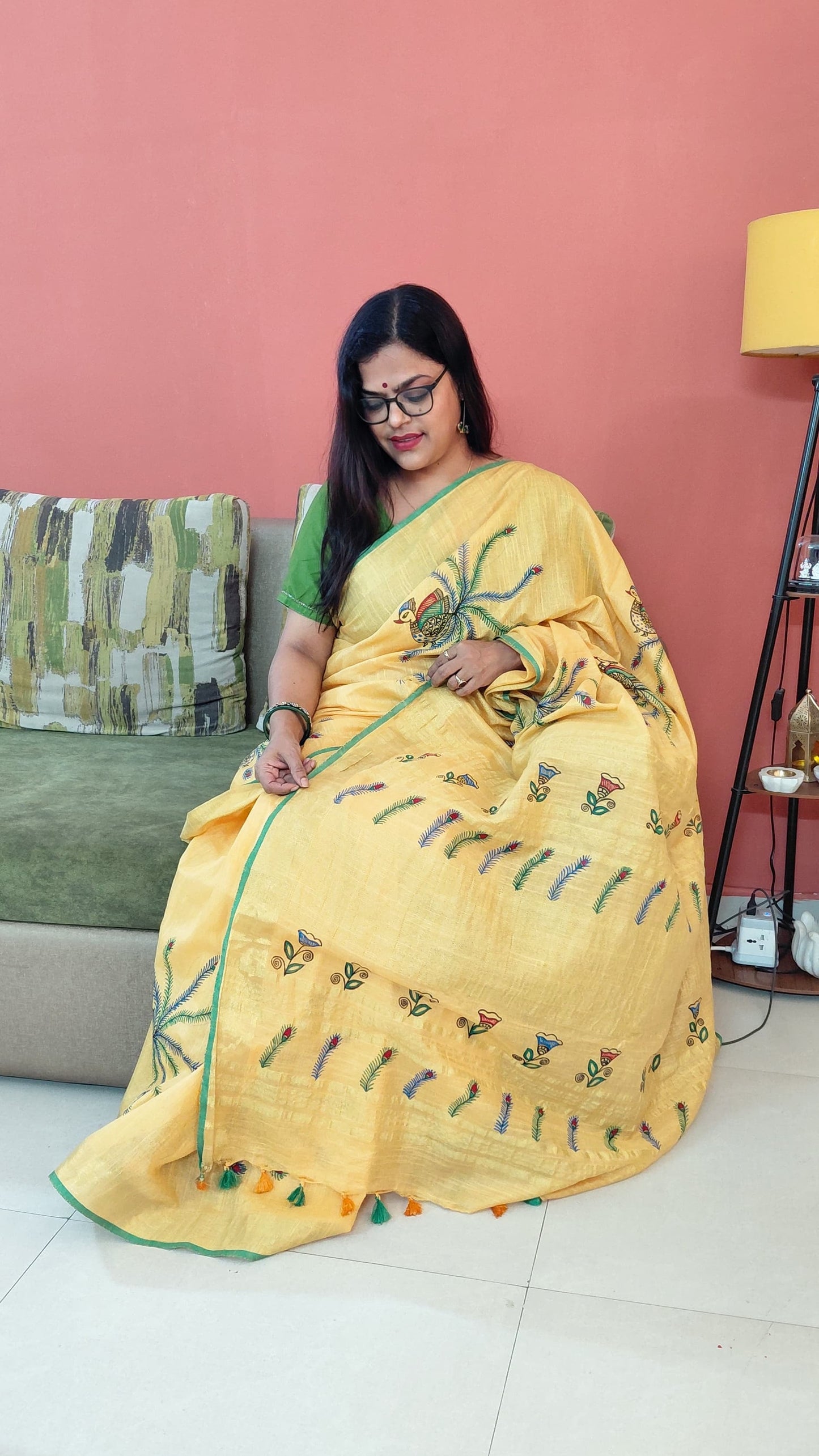 Model wearing yellow saree with hand-painted peacock design sitting pose